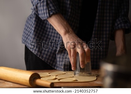 Dough rolling process. A man in a plaid shirt rolls out the dough with a rolling pin and cuts out the dough with a dumpling glass