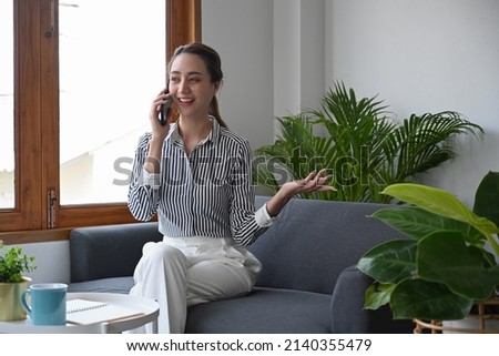Attractive young woman having cell phone conversation while sitting on couch at home.