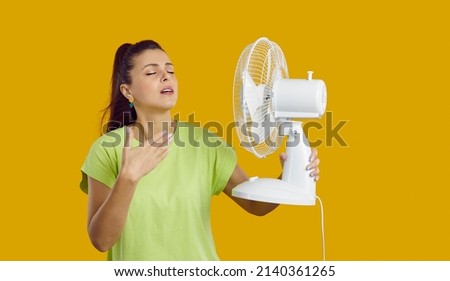 Young woman with a fan in her hand is exhausted from the heat, trying to cool off by the fan, oppressive heat, too hot weather and sultriness in summer, flat without air-conditioner concept. Royalty-Free Stock Photo #2140361265