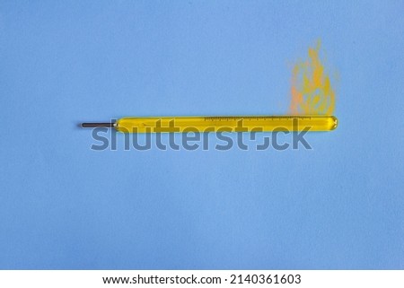 Vintage yellow mercury thermometer with fire painted on top on colorful paper background. Temperature and conceptual photography.
