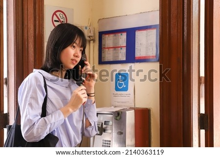happy young girl talking on traditional red fixed land line pay telephone