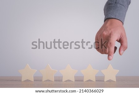 Businessman hand finger point at Five wooden stars on table. Rating evaluation concept. High satisfaction. Good reputation. Popularity rating of restaurants. Highest score. Service quality feedback.