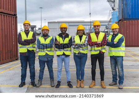 Multi-racial industrial workers happy looking at camera inside an international port terminal with containers in the open air. Focus on the face of the Indian man holding a tablet. Royalty-Free Stock Photo #2140371869