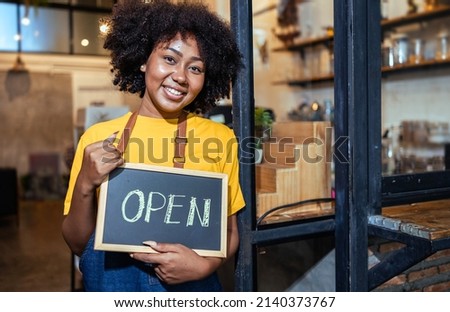 Young Female manager in restaurant with digital tablet or notebookWoman coffee shop owner with face mask hold open sign .Small business concept.