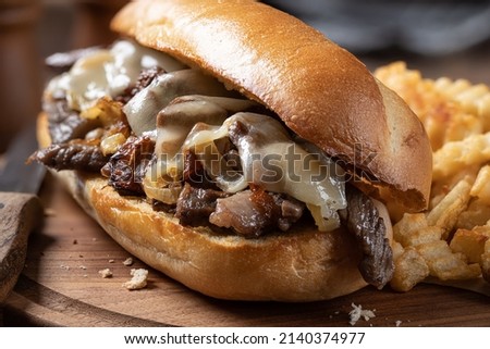 Philly cheesesteak sandwich made with steak, cheese and onions on a toasted hoagie roll with french fries on a wooden board Royalty-Free Stock Photo #2140374977