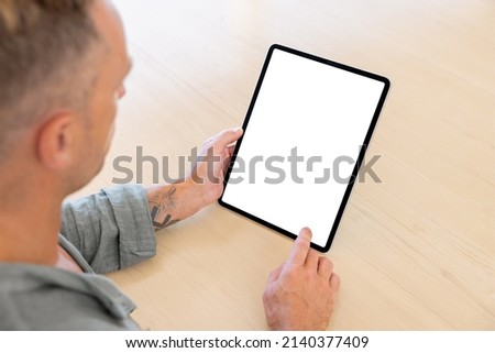Man using tablet computer, empty white screen mockup, over the shoulder view