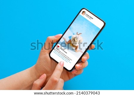 Woman viewing social media app on cell phone, looking at someone's shared vacation photo Royalty-Free Stock Photo #2140379043