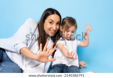 Picture of happy young woman mother with her little girl child daughter sitting isolated over blue background.