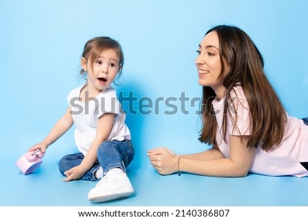 Picture of happy young woman mother with her little girl child daughter sitting isolated over blue background.