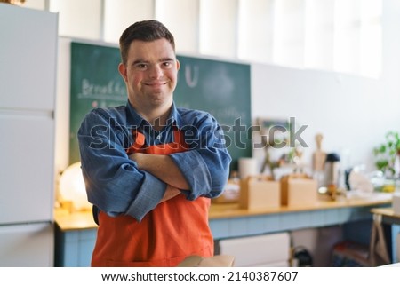 Cheerful young Down Syndrome waiter working in take away restaurant, social inclusion concept. Royalty-Free Stock Photo #2140387607