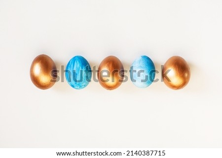 Frame of Easter colorful blue and golden color eggs on white background. Stylish trendy gold chocolate egg set isolated. Flat lay, top view, place for text. Happy egg hunt for kids concept