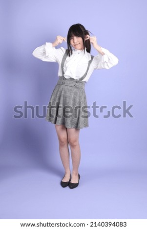 The cute young Asian girl with white preppy dressed style standing on the purple background