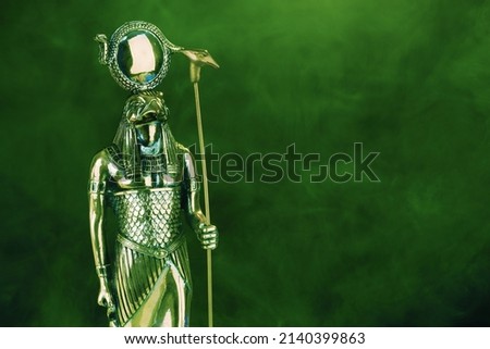 golden statue of the Egyptian god Ra with the head of a falcon on a black background with green illumination. High quality photo