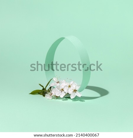 Spring Easter concept with paper egg shape decorated with fresh natural white cherry blossoms on blue green background. Minimal seasonal card design. 