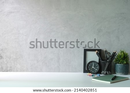 Stylish workplace with picture frame, stationery and potted plant on white table. Copy space.