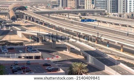 Futuristic building of Dubai metro station and luxury skyscrapers behind in Dubai Marina aerial timelapse. Traffic on Sheikh Zayed road highway overpass near parking lot, United Arab Emirates