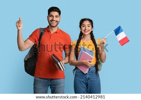 Study In France. Happy Arab Man And Woman Holding Workbooks And French Flag, Smiling Middle Eastern Students With Backpacks Posing Over Blue Studio Background, Recommending Study Abroad, Copy Space Royalty-Free Stock Photo #2140412981