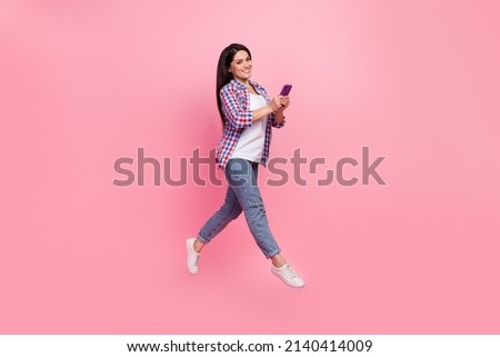 Full size photo of mature brunette lady run hold telephone wear shirt jeans footwear isolated on pink background