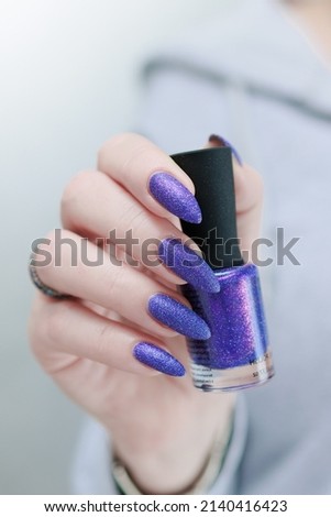 Female hand with long nails and purple plum blue manicure holds a bottle of nail polish