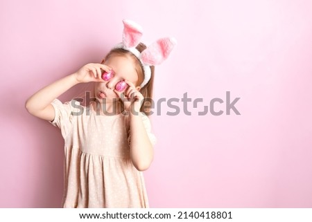 Happy Easter. The cheerful girl hid her eyes behind the colored shiny eggs in her hands. Pink background. Space for text. Pranks. Emotions. High quality photo