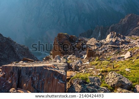 Sunny mountain view from cliff at very high altitude. Scenic alpine landscape with beautiful sharp rocks and couloirs in sunlight. Beautiful scenery on abyss edge with sharp stones and green grass. Royalty-Free Stock Photo #2140424493