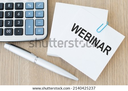 A white business card with webinar text stands on a desk next to a calculator