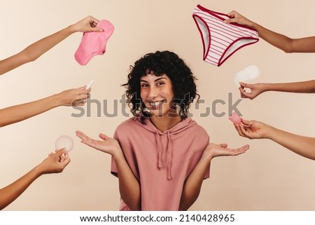 Reusable or non-reusable? Happy young woman smiling at the camera while surrounded by hands holding different sanitary products. Cheerful modern woman making a choice about her feminine hygiene. Royalty-Free Stock Photo #2140428965
