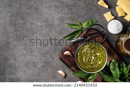 Pesto sauce and ingredients. Italian green basil pesto in a gravy boat garnished with pine nuts. Layout on gray kitchen table with copy space Royalty-Free Stock Photo #2140431433