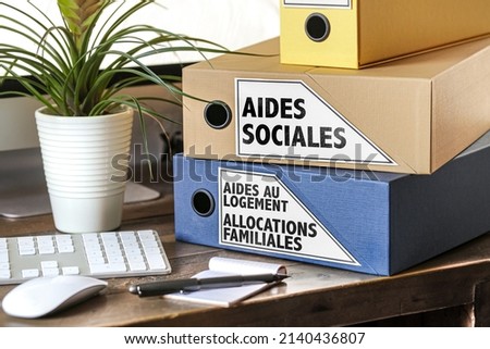two binders with the french words that means social assistance, family allowances and housing assistance on an office Royalty-Free Stock Photo #2140436807
