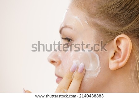 Young woman applying cream cosmetic, mask moisturizing to her face. Beauty treatment. Skincare.