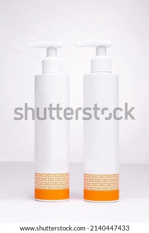 two white bottles for cosmetics with an orange pattern on a white background.