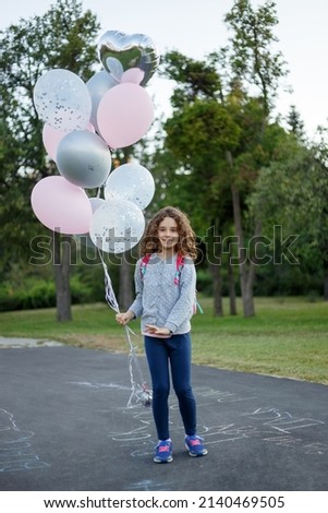 Full length image of an adorable cute schoolgirl in a park playing and holding a ballons in the park.