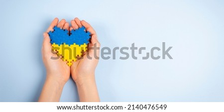 Child hands holding Ukraine flag colors heart on light blue background. Top view