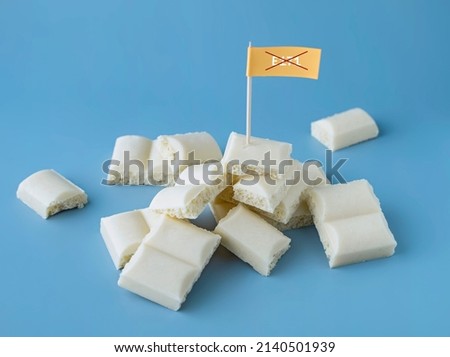Heap of white chocolate cubes with the sign of a dangerous additive e171 on a blue background