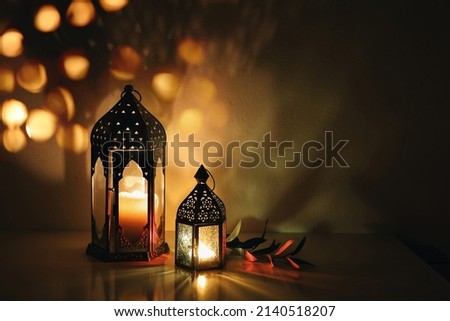 Decorative Arabic lanterns with burning candles at night. Glittering golden bokeh lights. Festive greeting card, invitation. Muslim holy month Ramadan Kareem, dark background with olive branch. Royalty-Free Stock Photo #2140518207
