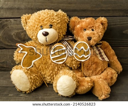 Decorative postcard on a wooden background, brown fluffy teddy bears sit in their paws with Easter cookies, a rabbit and eggs.  Holiday atmosphere.  The concept of a bright Easter holiday.