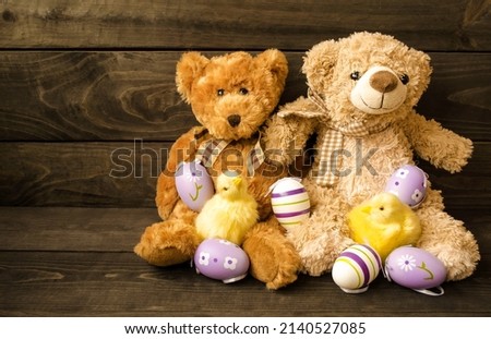 Decorative postcard, soft fluffy teddy bears with Easter eggs and yellow little chickens sit on a wooden background.  Concept holiday bright easter, minimalism.  Space for copy text.