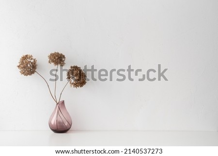White desk with minimal vase with a decorative dried branches, flower against white wall.	
