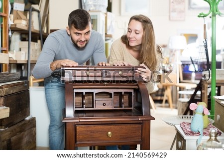 Happy girl with boyfriend choosing vintage cabinet in furnishings store Royalty-Free Stock Photo #2140569429
