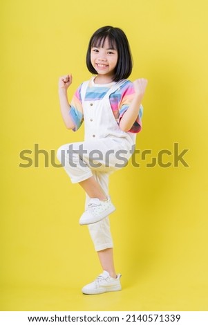 Full length image of Asian child posing on yellow background Royalty-Free Stock Photo #2140571339
