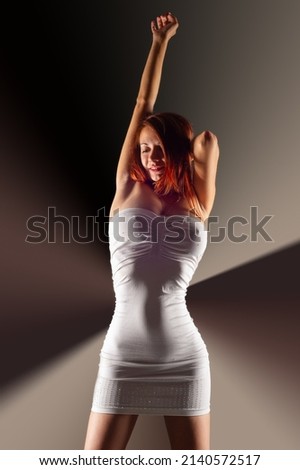 The girl is dancing in the backlight. The girl is wearing tight white dresses. Red hair. bare feet