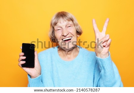 lifestyle, tehnology and people concept: Elderly lady holding a smartphone and making v-sign