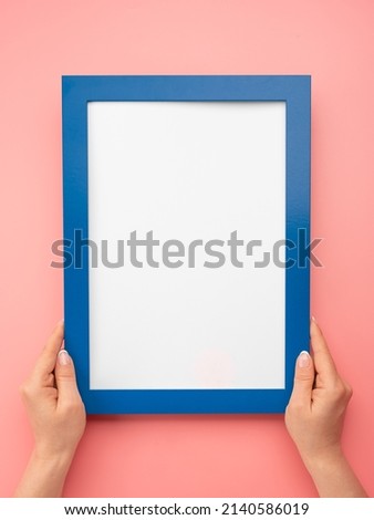 Woman hold blank diploma frame on pink wall background. Female hands hold empty blue mockup frame. Cropped hand of woman holding diploma frame against pink wall. copy space. vertical image