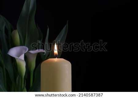 Close up of candle burning flame in the darkness and arum lilies illuminated by the candlelight alongside in a conceptual image Royalty-Free Stock Photo #2140587387