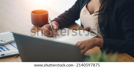 Closeup image of businesswoman hand writing note and working on laptop computer at office.