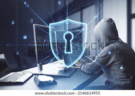 Side view of hacker at desktop using computers with creative glowing web security shield on blurry office interior background. Secure information concept. Double exposure
