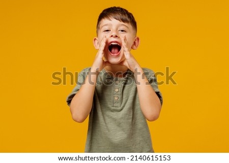 Little small smiling happy boy 6-7 years old in green t-shirt scream hot news about sales discount with hands near mouth isolated on plain yellow background. Mother's Day love family lifestyle concept