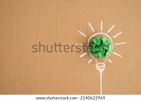 CSR (Corporate Social Responsibility ) in business, creative ideas imagination concept. Flat lay of green crumpled paper light bulb ball with drawing on recycle parcel paper box background copy space.