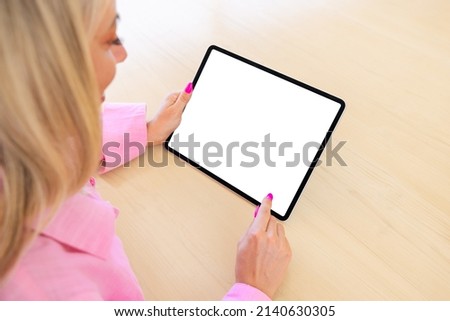 Woman using tablet computer, empty white screen mockup, over the shoulder view