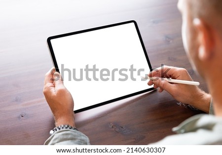 Man using tablet computer with stylus pen, empty white screen mockup, over the shoulder view